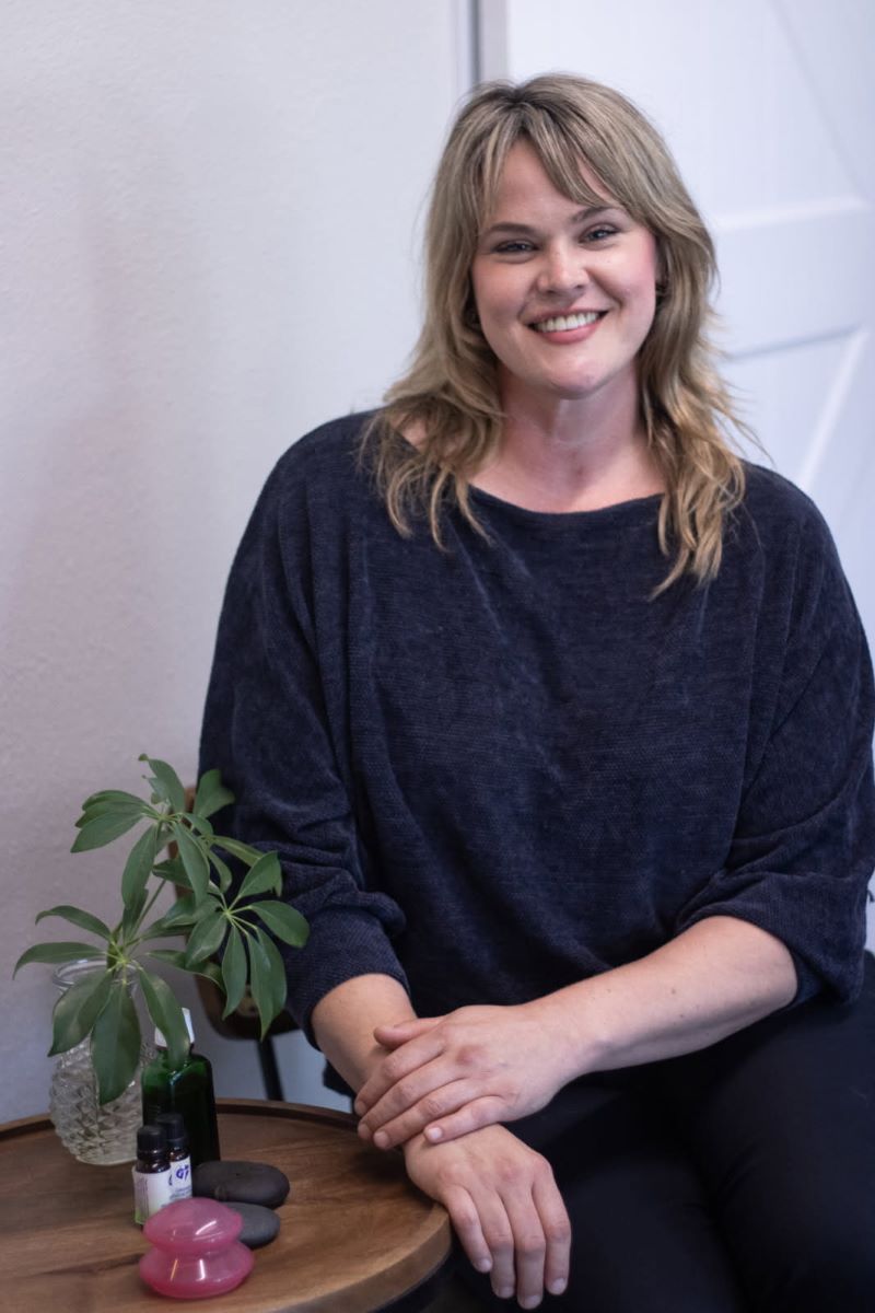 Hillary sitting next to a table with a green plant. She is smiling, inviting you to speak with her.