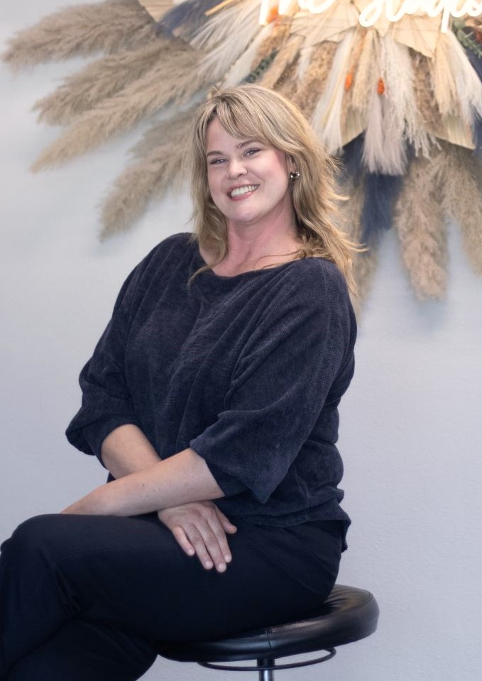 Massage therapist posing on a stool, arms crossed, smiling.